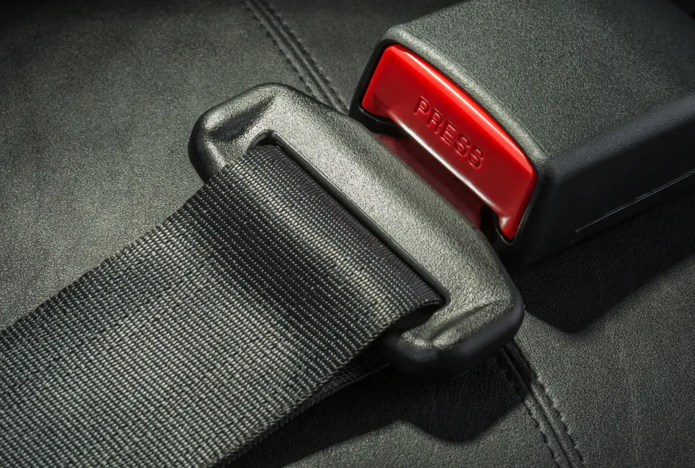A retractable seatbelt assembly showing webbing entering a moulded latch plate beside its buckle receiver.