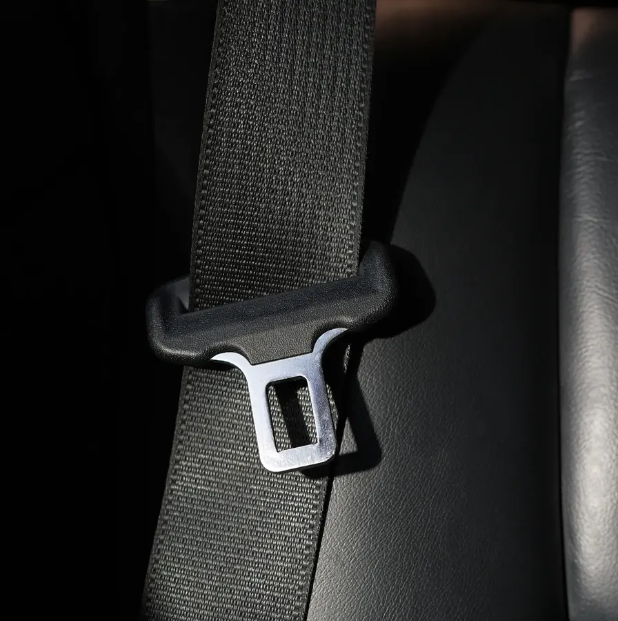 Seatbelt webbing running through a moulded guide with a metal latch plate attached, photographed against a dark vehicle interior.